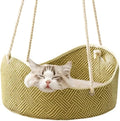 Green rattan cat hammock with metal hooks hanging on a white fence, a cat lounging inside.