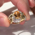 Gold-colour women's ring with an embossed feather design and a central yellow zircon stone on a finger.