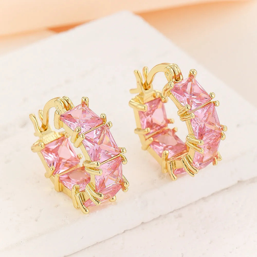 Women's geometric U-shaped gold earrings with round black zircon crystals on white background
