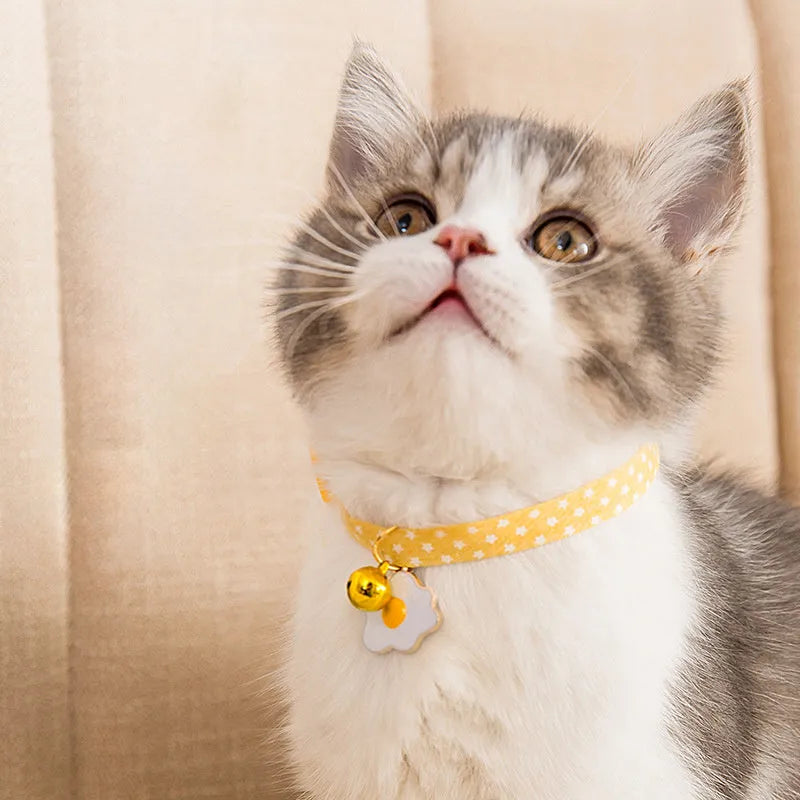 Adjustable green cat collar with a silver bell and pink bow tie on a white background.