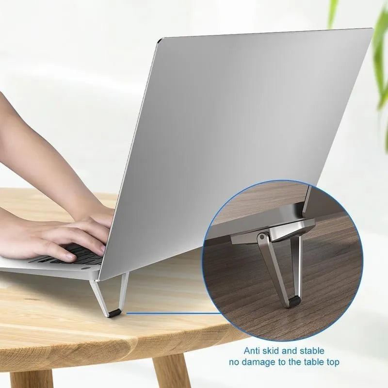 Small silver foldable aluminum laptop stand bracket with 3M adhesive strips on a white background.