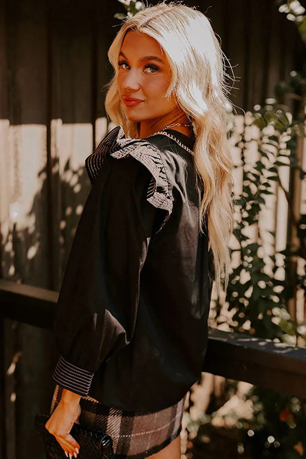 Black women's V-neck blouse with long ruffle sleeves and contrast white stitching on seams.