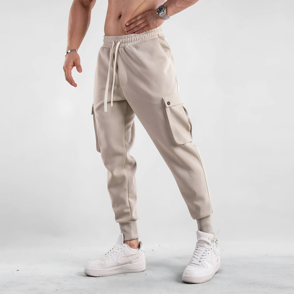 Men's loose light grey cotton trousers with ankle ties and multiple pockets laid flat.
