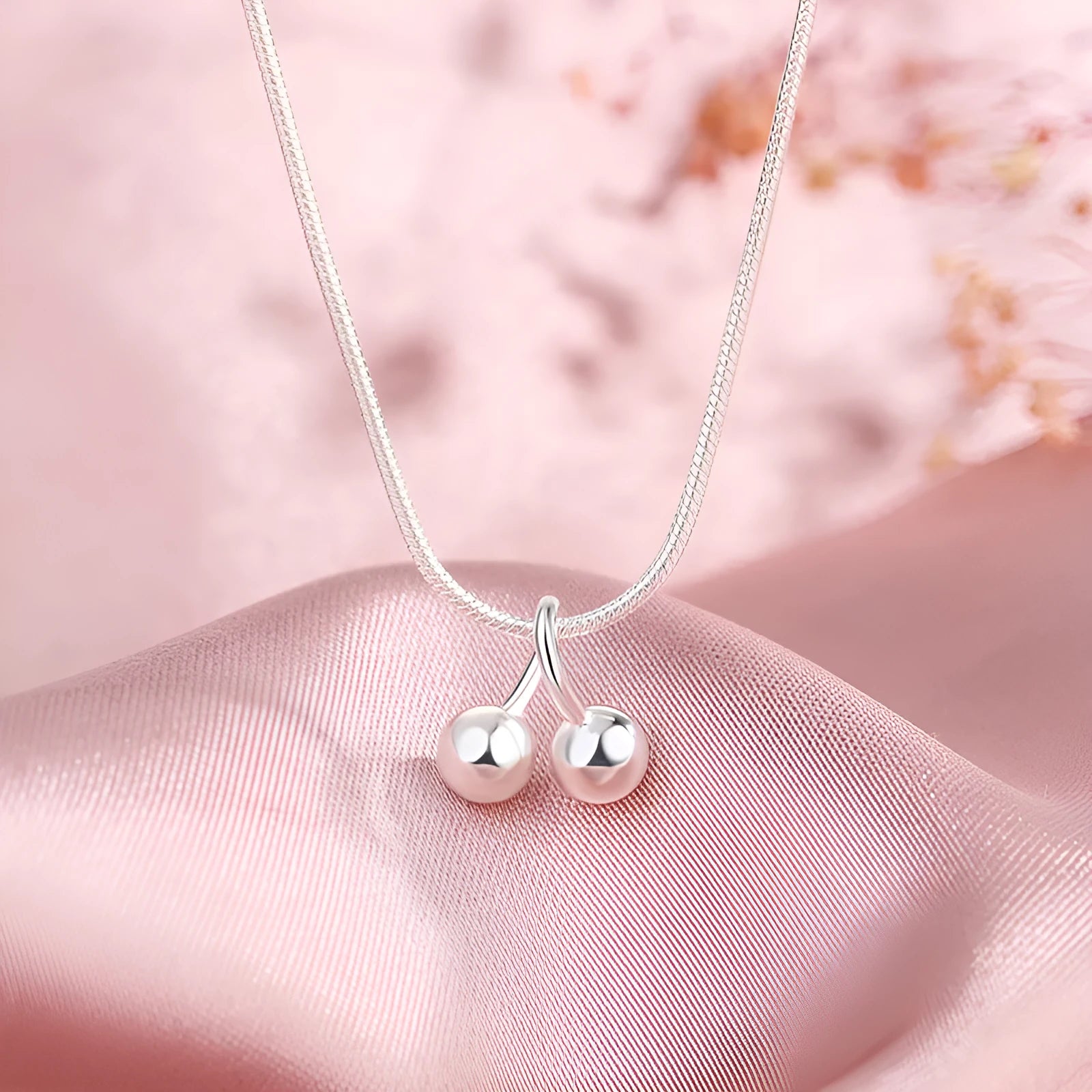 Silver cherry necklace for women with adjustable snake bone chain on a grey background.