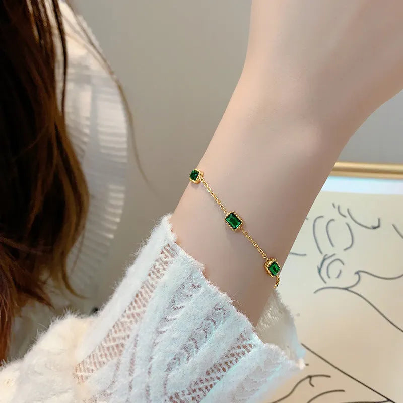 Titanium steel emerald zircon necklace and bracelet set with gold hardware and O-ring chain on a white background
