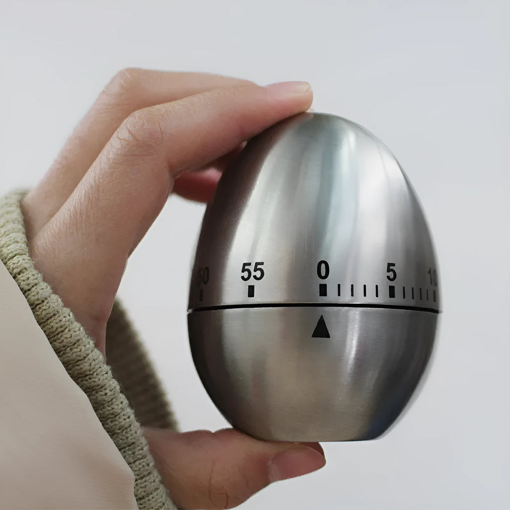 Stainless steel egg-shaped mechanical kitchen timer on a kitchen worktop.