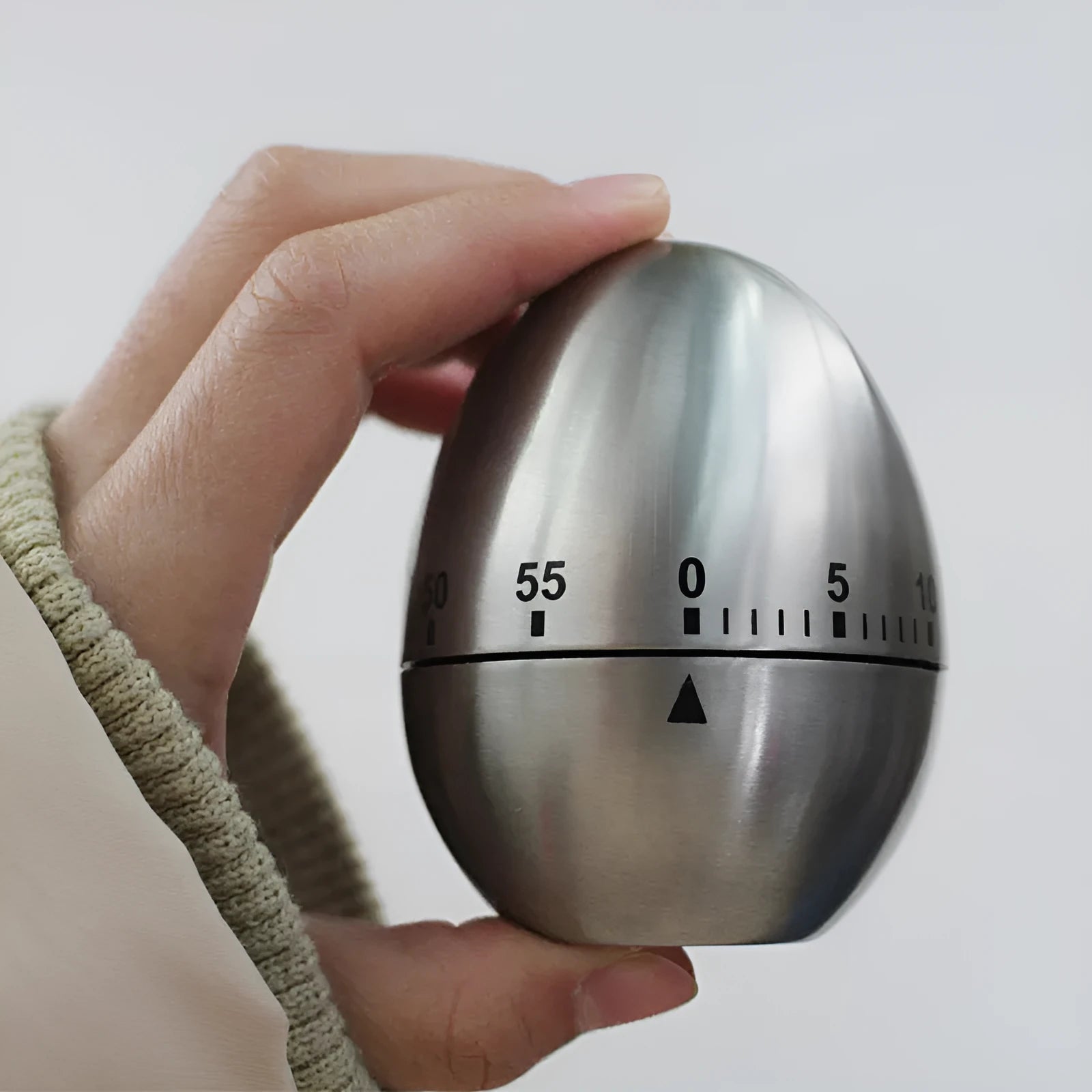 Stainless steel egg-shaped mechanical kitchen timer on a kitchen worktop.