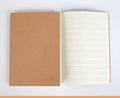Beige softcover thread-bound notebook in 16K size lying open on a table, showing grid paper inside.