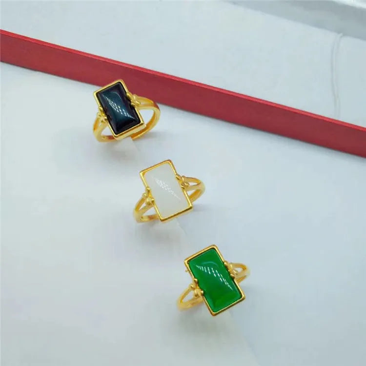 Adjustable gold-plated brass ring with a black artificial gemstone on a neutral background.
