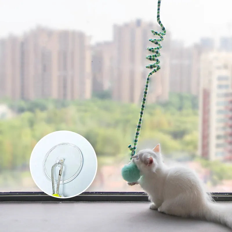 Spring-mounted inflatable ball cat toy with bell, attached to a door via a clear suction cup.