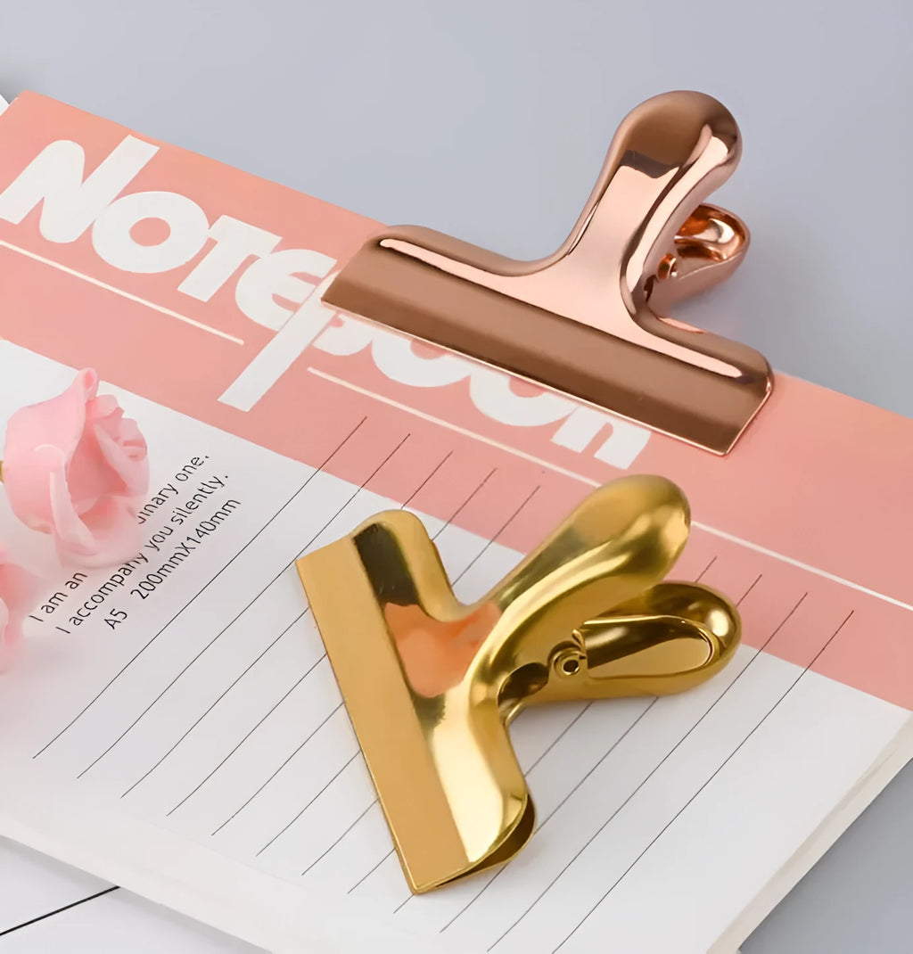 Gold stainless steel dovetail clip holding a stack of papers on a desk