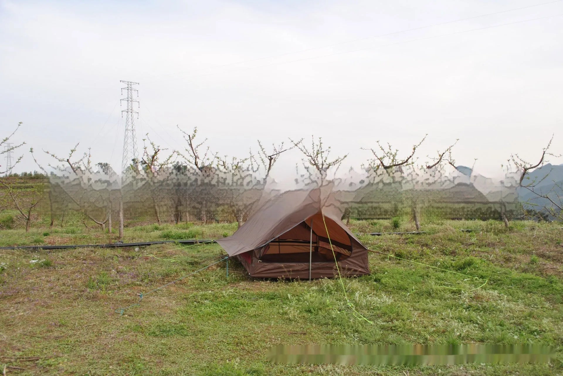 Brown ultralight A-frame hiking tent pitched with hiking poles in an outdoor setting