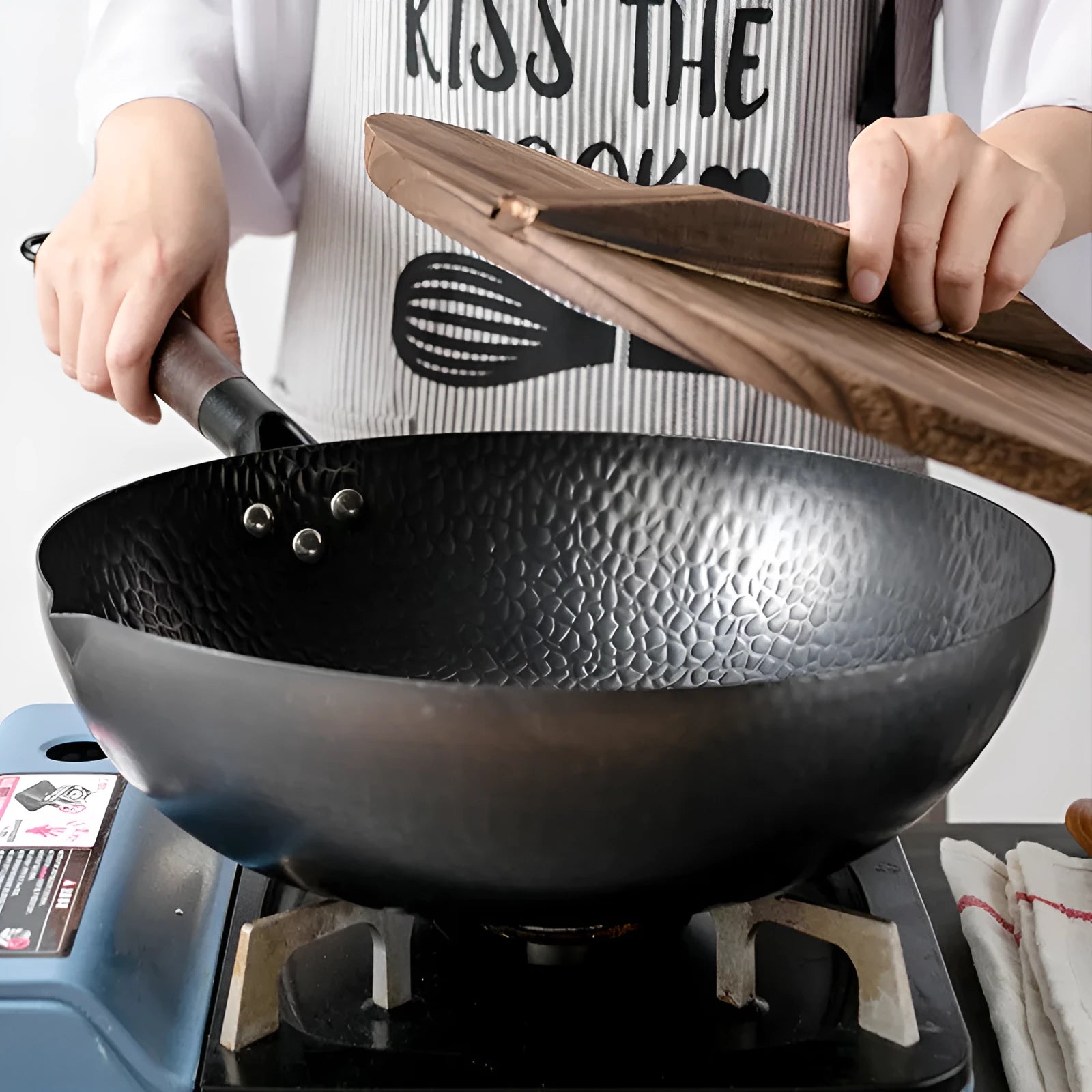 Handmade traditional black iron wok with a wooden handle, shown with a glass lid.