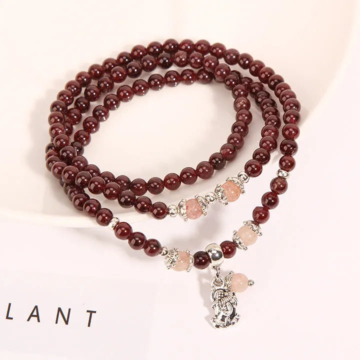 Wine red garnet crystal bracelet with flower-shaped charm on a model's wrist.