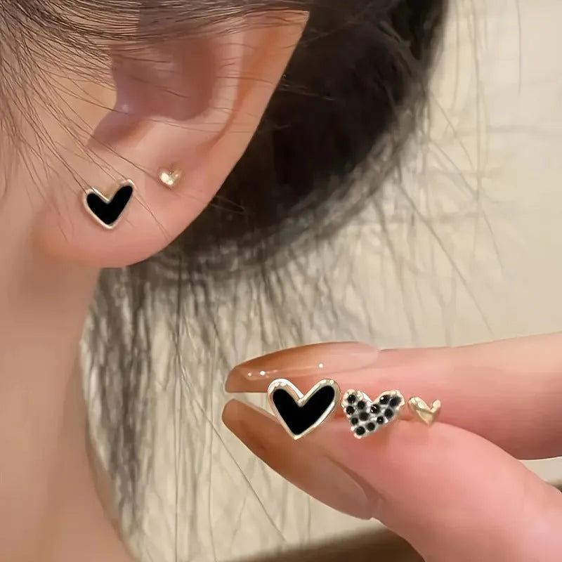 Three pairs of women's heart-shaped alloy earrings in gold, black, black and white, and pink colours