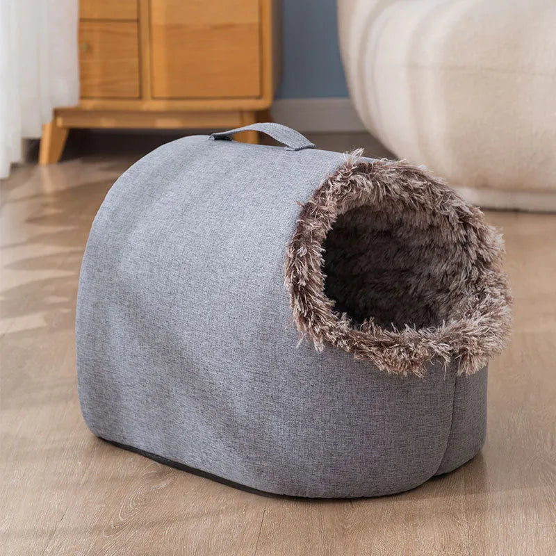 Grey fleece-lined closed cat sleeping bag with portable handle on brown floor