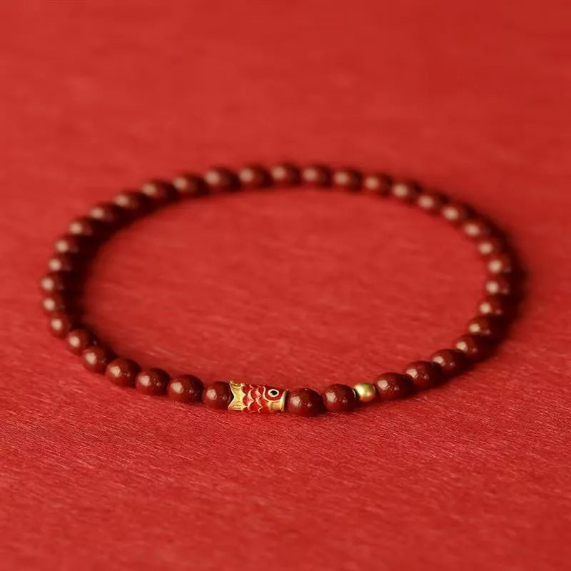Handmade natural cinnabar koi bracelet with gold balls on a bead, showing traditional Chinese style.