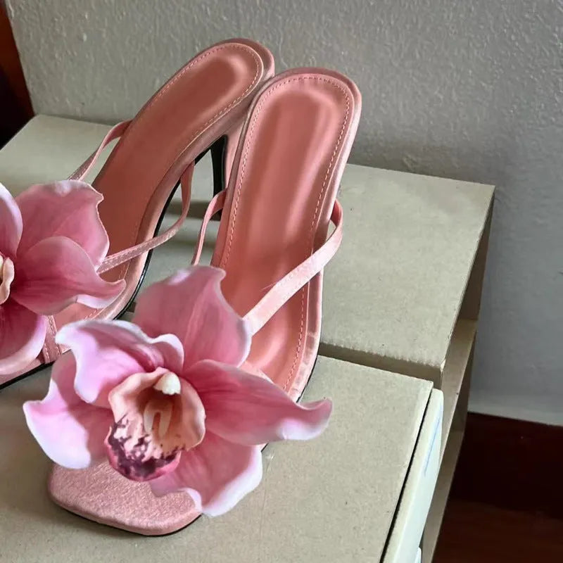 Pink women's sandals with a satin upper, artificial white Phalaenopsis flower, square toe, and a mid heel.