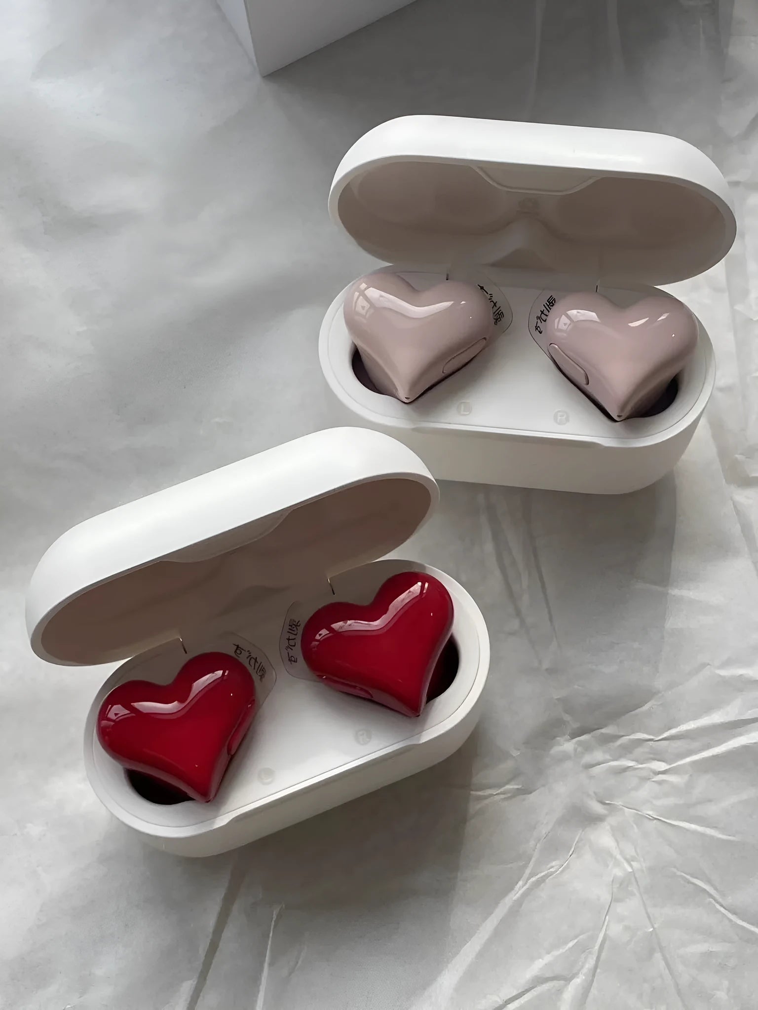 Heart-shaped wireless Bluetooth headphones in red or pink with in-ear design and charging cable