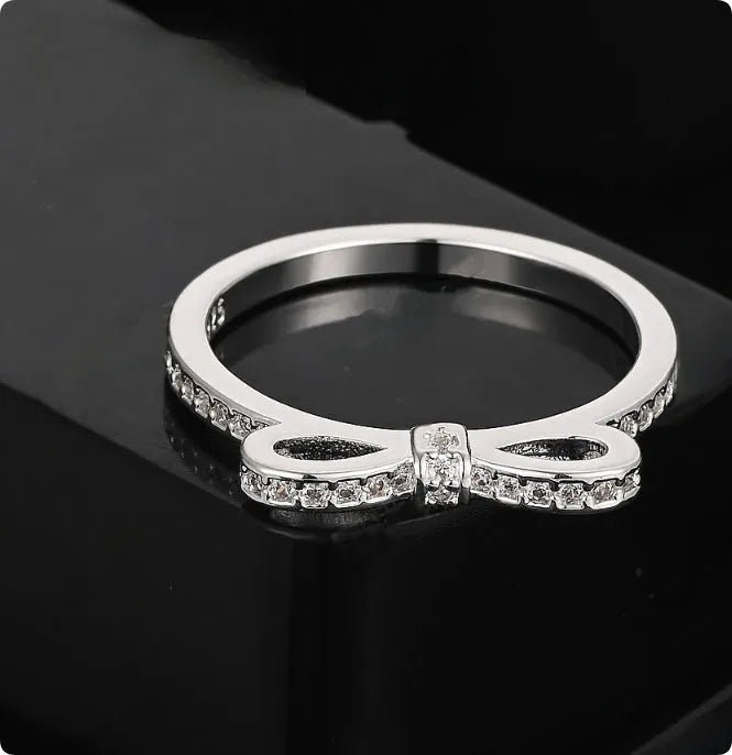 Silver coloured bow-shaped ring with sparkling rhinestone zircon crystals on a finger.