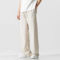 Men's beige loose straight-leg linen trousers with a drawstring waist, shown in a casual summer setting.
