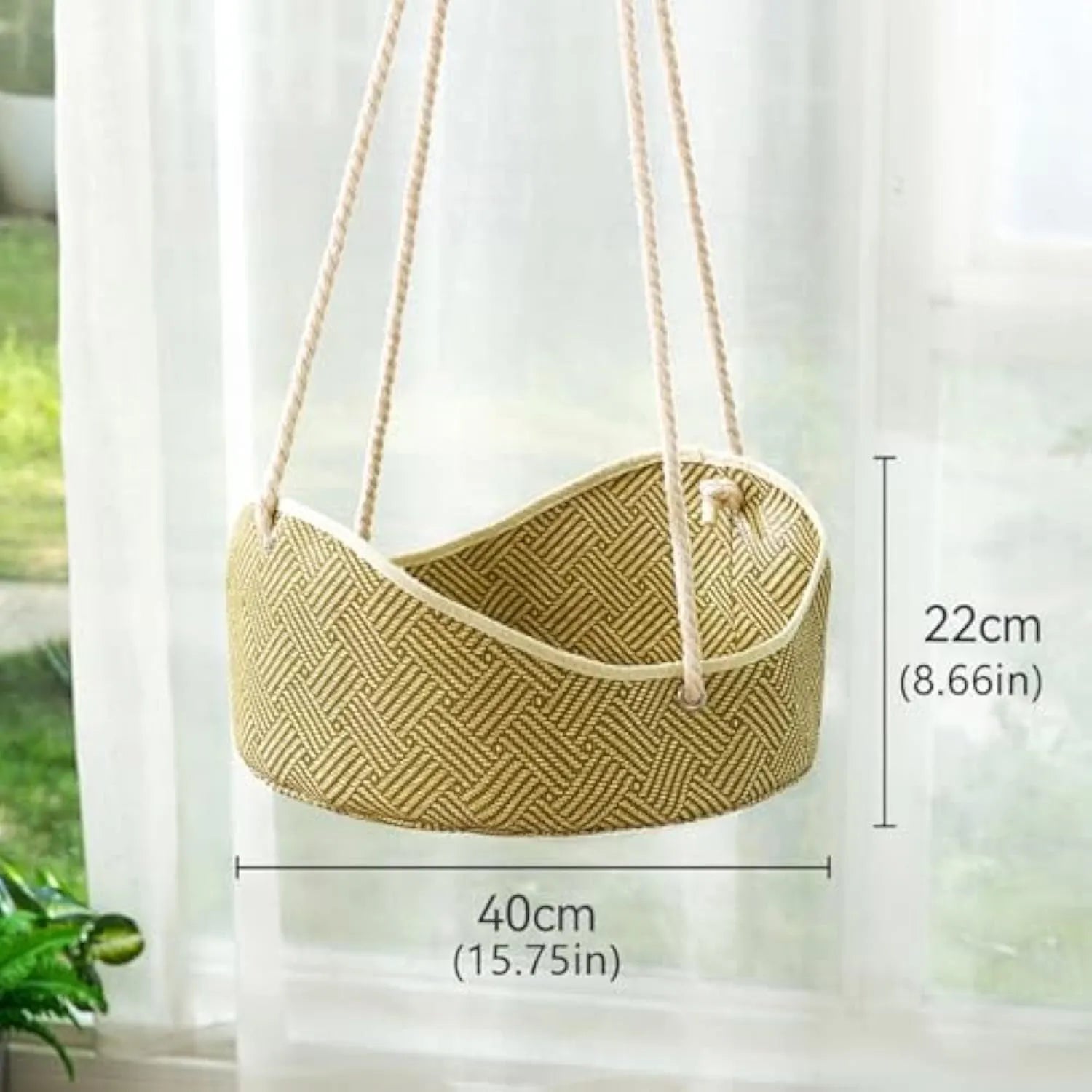 Green rattan cat hammock with metal hooks hanging on a white fence, a cat lounging inside.