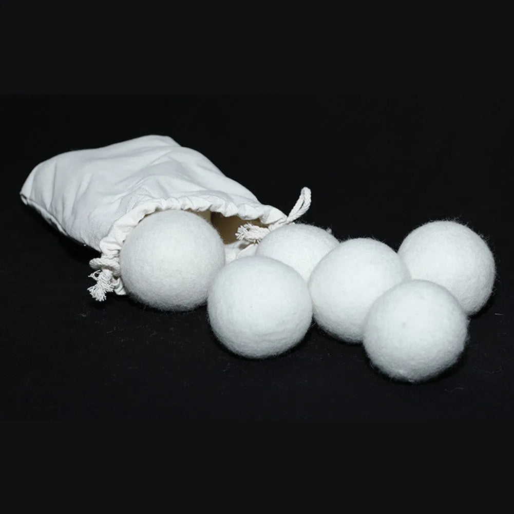 A white wool felt drying ball for laundry next to a plain cotton storage bag on a blue background.