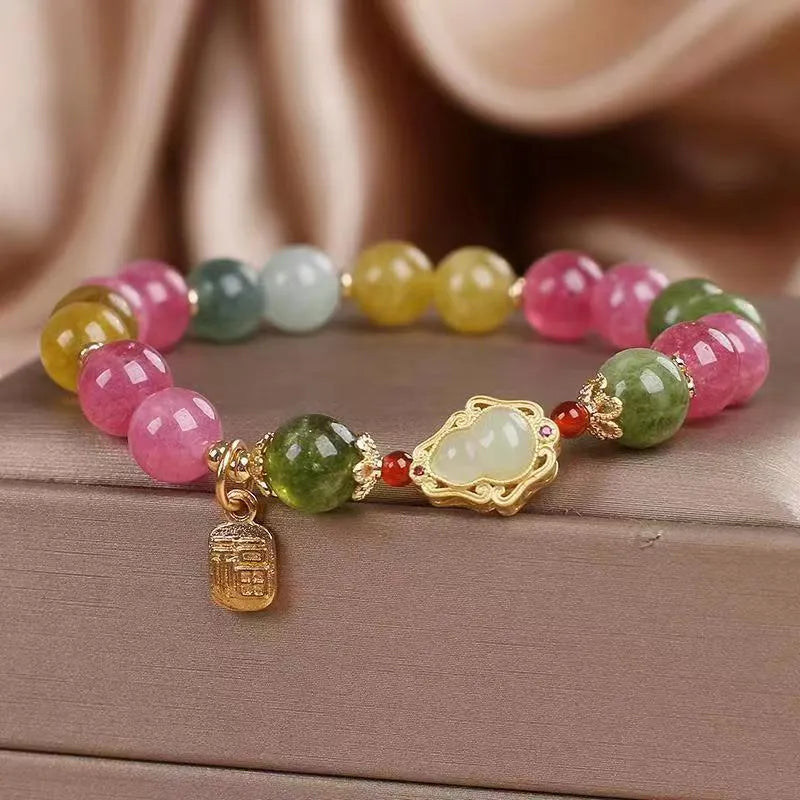 Women's bracelet with colourful tourmaline gourd blessing charm and floral clasp on a mixed material chain.