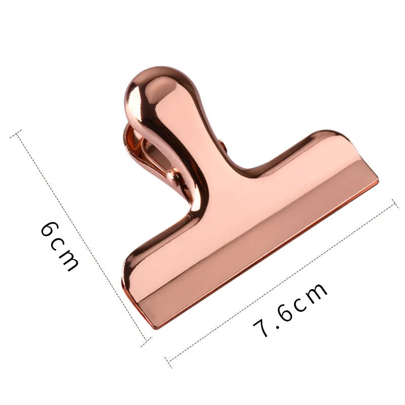 Gold stainless steel dovetail clip holding a stack of papers on a desk