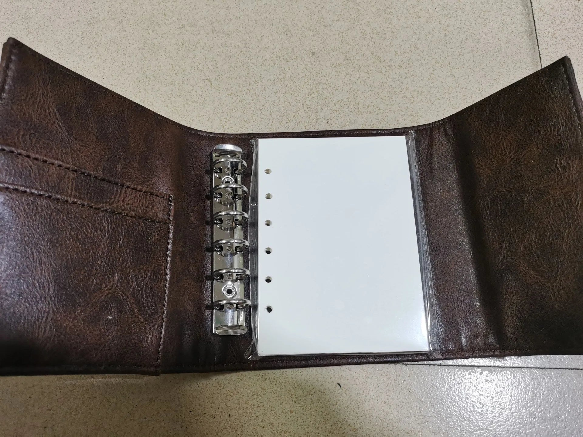 Brown A7 retro notebook with buckle closure showing loose-leaf binding and raw wood pulp paper