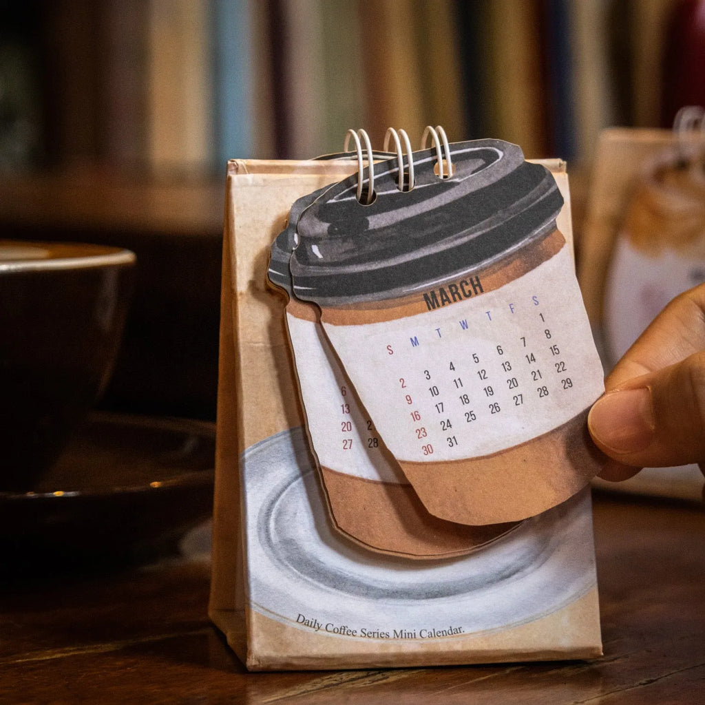 Small 2025 mini desk calendar open to a daily page, showing modern simple design on a desk.