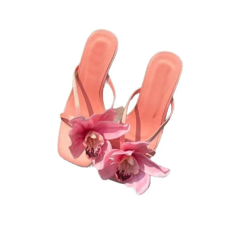 Pink women's sandals with a satin upper, artificial white Phalaenopsis flower, square toe, and a mid heel.