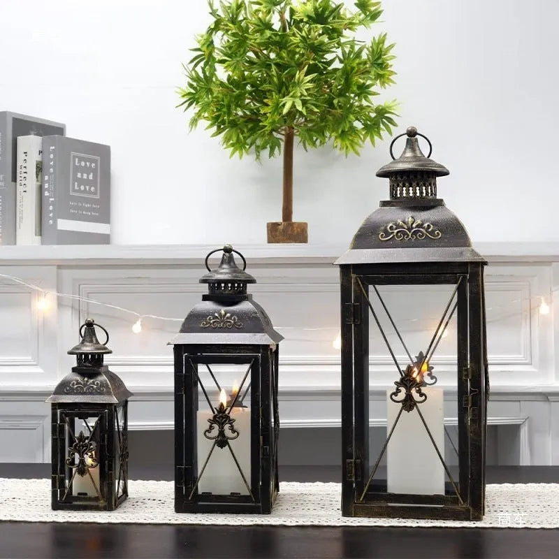Black gold wrought iron floor standing storm lantern with tempered glass panels on a stone patio.