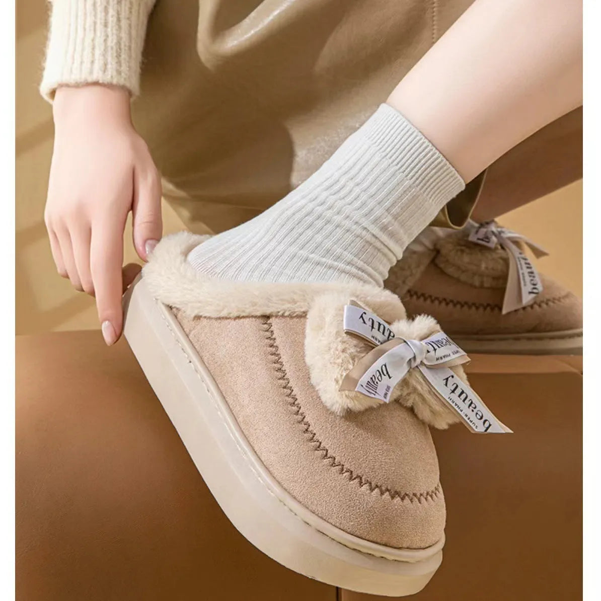 Beige women's suede half slippers with a black ribbon bow and thick cotton sole.
