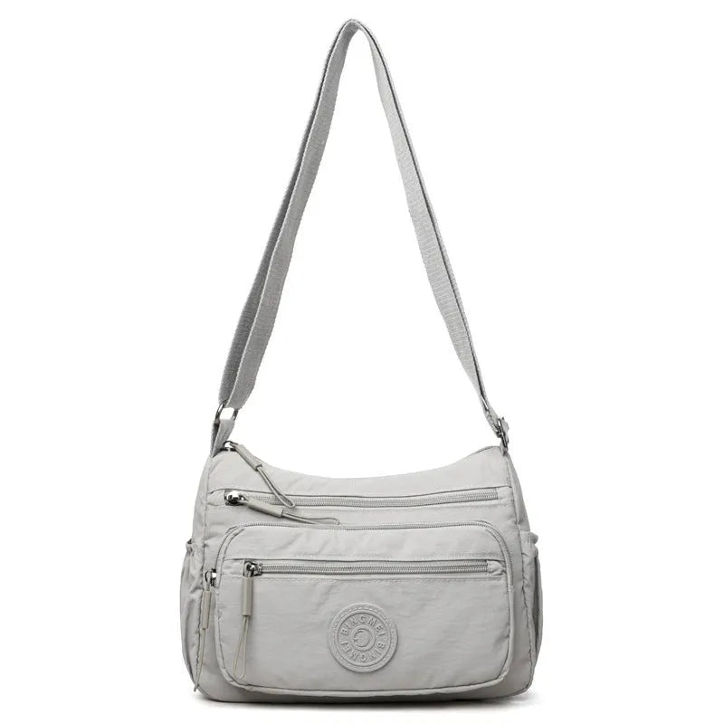 Grey water-repellent nylon crossbody bag showing front three-dimensional pocket and adjustable shoulder strap.