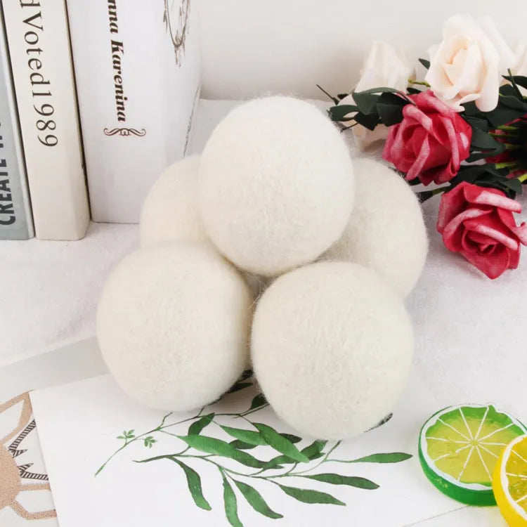 A white wool felt drying ball for laundry next to a plain cotton storage bag on a blue background.
