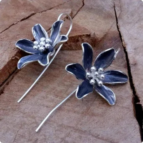 A pair of purple flower-shaped alloy stud earrings with a simple post back, shown against a plain background.