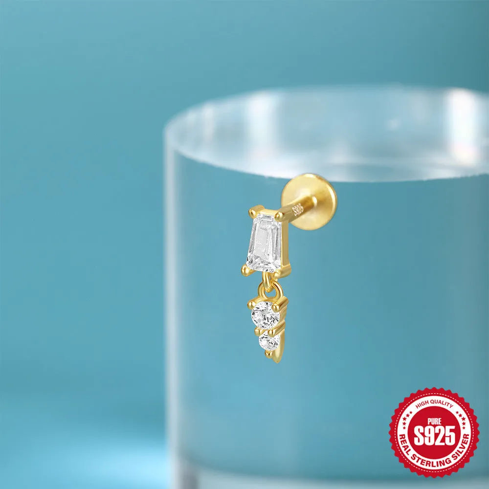 Close-up of a gold-coloured S925 sterling silver ear stud with a XINGX pattern inlay and a thin dangling tassel.