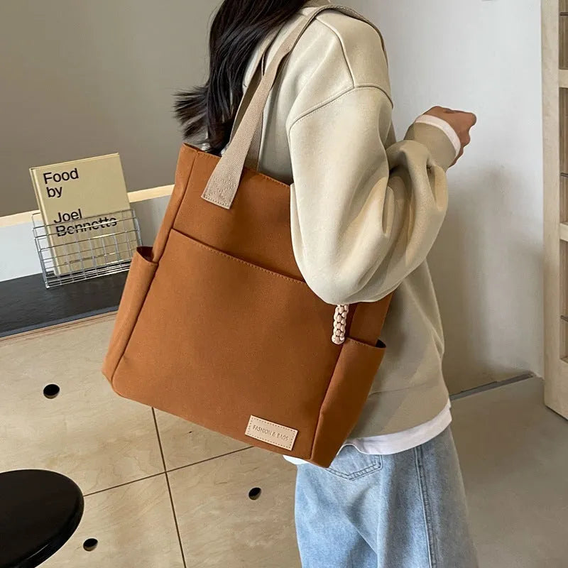 Women's large canvas satchel in beige with shoulder strap, horizontal square shape, and visible sewing thread details