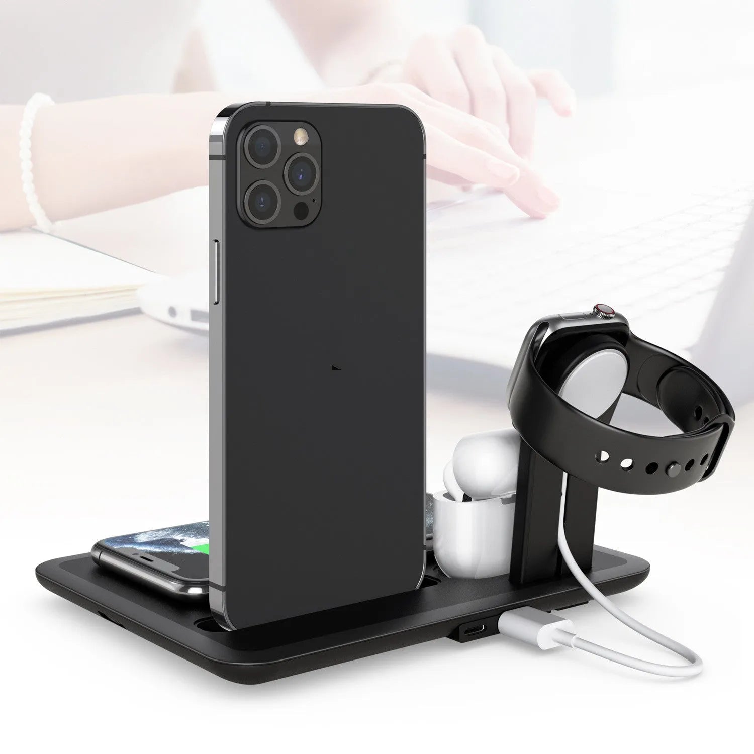 Black multi-device wireless charging stand holding a phone, headphones, and a smartwatch on a desk.