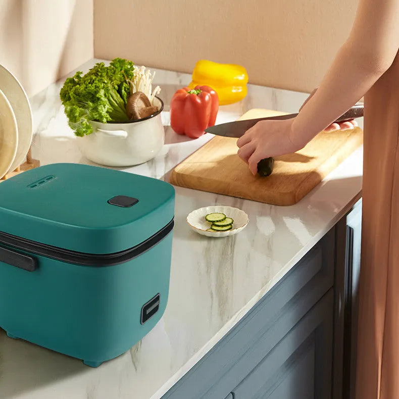 Green 1.2L mini rice cooker with metal body, button controls, and steaming plate on a worktop.