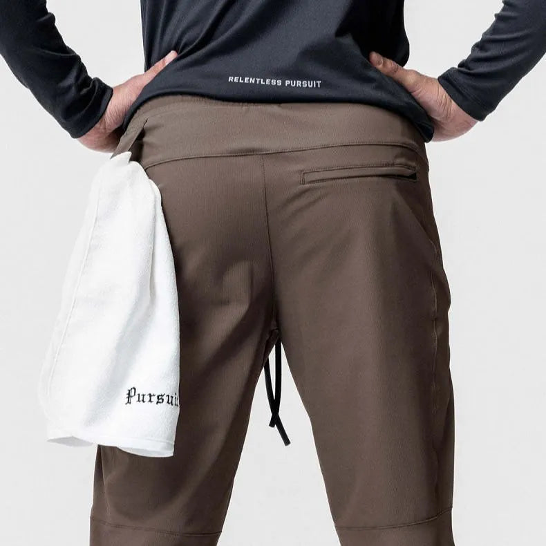 Man wearing loose grey running trousers with tied ankles, made from quick-dry polyester fabric.