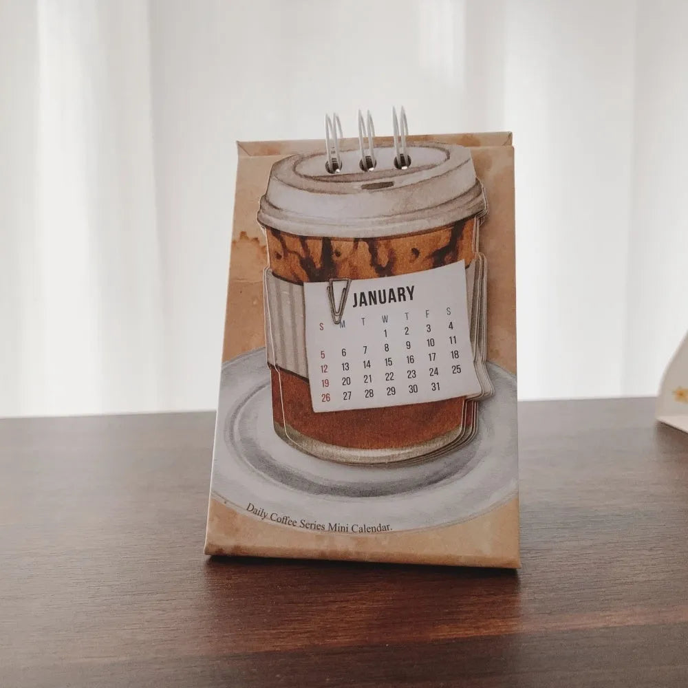 Small 2025 mini desk calendar open to a daily page, showing modern simple design on a desk.