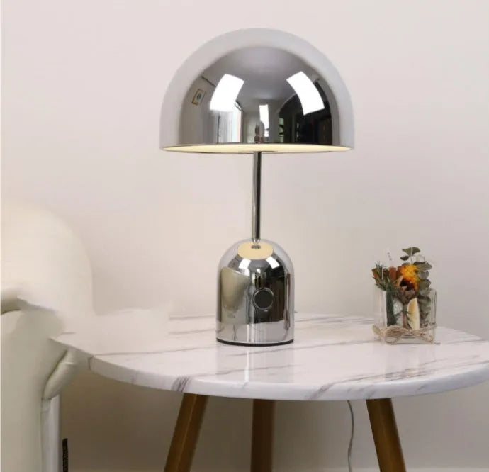 Modern mushroom table lamp with metal base in rose gold finish on a wooden table.