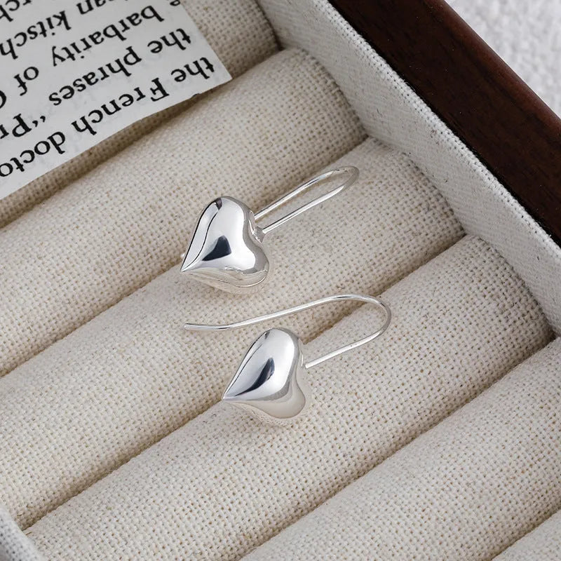 Silver coloured heart-shaped earrings with three-dimensional design and ear hooks