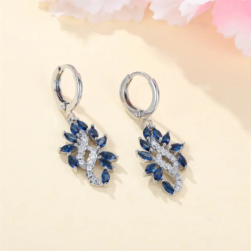 A pair of platinum sapphire blue alloy drop dangle earrings for women on a plain background.