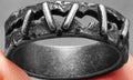 Close-up of a stainless steel double ring with dark punk stitching style, shown on a finger.
