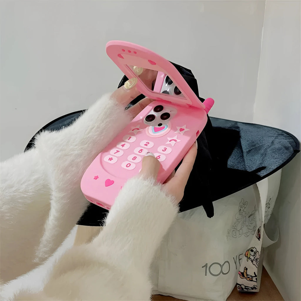 A light pink silicone iPhone case shaped like a flip phone with a built-in mirror on the front.