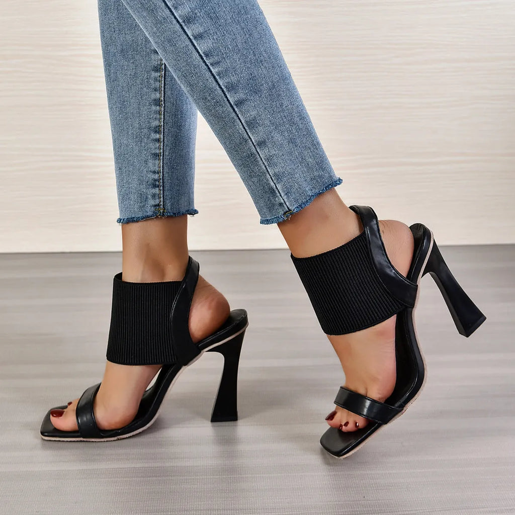Women's black high heel sandals with a crossing elastic strap and a rubber sole.