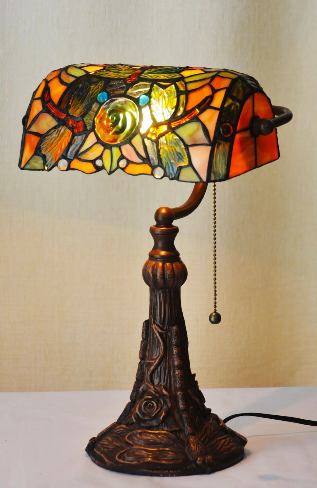 Tiffany-style desk lamp with coloured stained glass shade and resin base on a wooden desk.